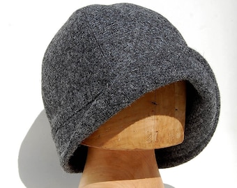 May include: A gray felt cloche hat with a rounded crown and a wide brim. The hat is sitting on a wooden hat form.
