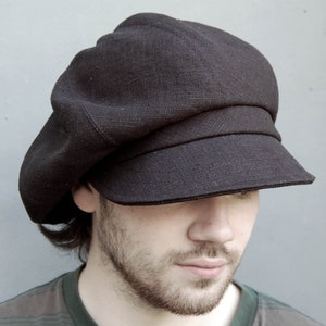 Könnte beinhalten: Eine schwarze Newsboy-Mütze aus Leinen mit breitem Schirm. Die Mütze wird von einer Person mit Bart getragen.