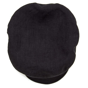May include: A black newsboy cap, featuring a rounded crown and a small, stiff brim. The cap is made from a textured fabric, and is a solid black colour. The material appears to be breathable, making it suitable for different weather conditions.