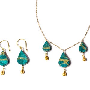 May include: A gold chain necklace with three teardrop-shaped pendants. The pendants are green with gold accents. Matching earrings with the same design are also included.