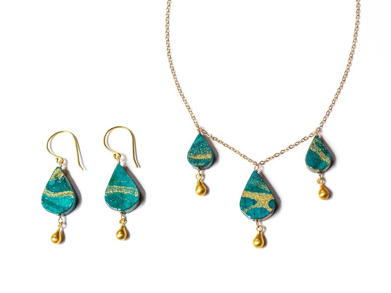 May include: A gold chain necklace with three teardrop-shaped pendants. The pendants are green with gold accents. Matching earrings with the same design are also included.