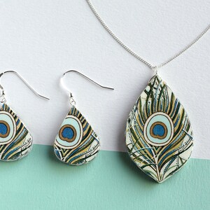 May include: A silver necklace and earrings set with teardrop-shaped pendants featuring a peacock feather design in shades of blue, green, and gold.