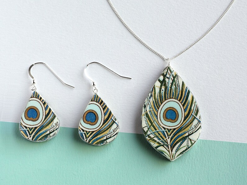 May include: A silver necklace and earrings set with teardrop-shaped pendants featuring a peacock feather design in shades of blue, green, and gold.