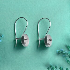 May include: A pair of silver earrings with a circular charm that reads "Choose You".
