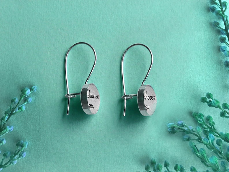 May include: A pair of silver earrings with a circular charm that reads "Choose You".