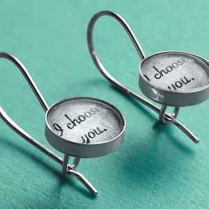 May include: A pair of silver earrings with a round, clear glass charm that says "I choose you."