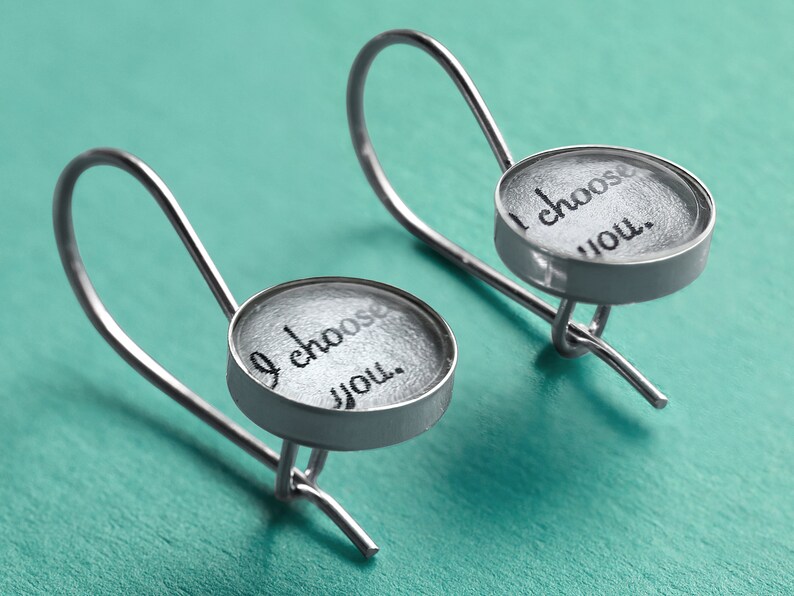 May include: A pair of silver earrings with a round, clear glass charm that says "I choose you."