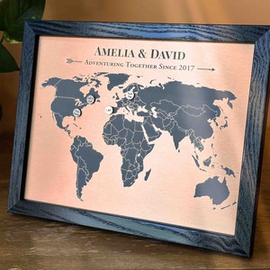 Peut inclure: Une carte du monde encadr&eacute;e avec un fond en cuivre et un cadre noir. La carte est marqu&eacute;e de punaises argent&eacute;es. Le texte "Amelia & David Adventuring Together Since 2017" est imprim&eacute; sur la carte.
