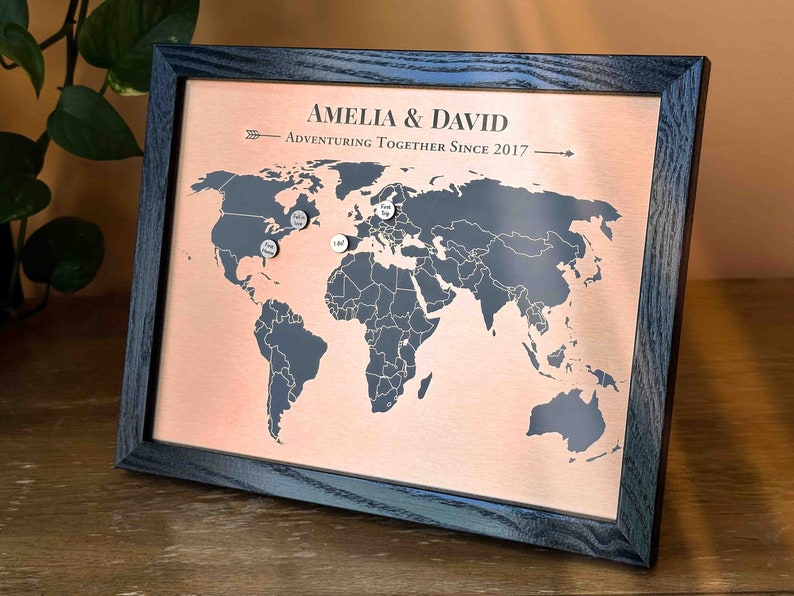 Peut inclure: Une carte du monde encadr&eacute;e avec un fond en cuivre et un cadre noir. La carte est marqu&eacute;e de punaises argent&eacute;es. Le texte "Amelia & David Adventuring Together Since 2017" est imprim&eacute; sur la carte.