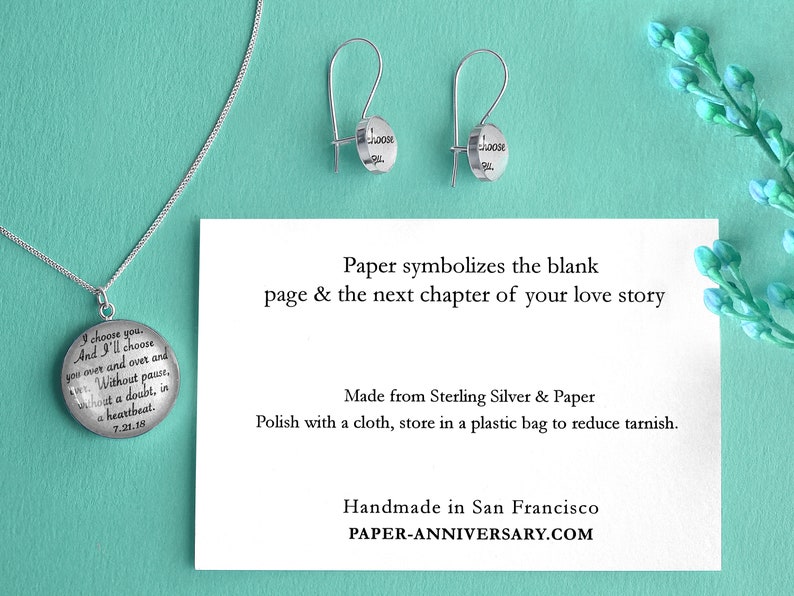May include: A silver necklace and earrings set with a round pendant and earrings that say "I choose you. And I'll choose you over and over and over. Without pause. Without a doubt, in a heartbeat. 7.21.19" and "I choose you". The jewelry is on a light blue background with a card that says "Paper symbolizes the blank page & the next chapter of your love story. Made from Sterling Silver & Paper. Polish with a cloth, store in a plastic bag to reduce tarnish. Handmade in San Francisco. PAPER-ANNIVERSARY.COM".