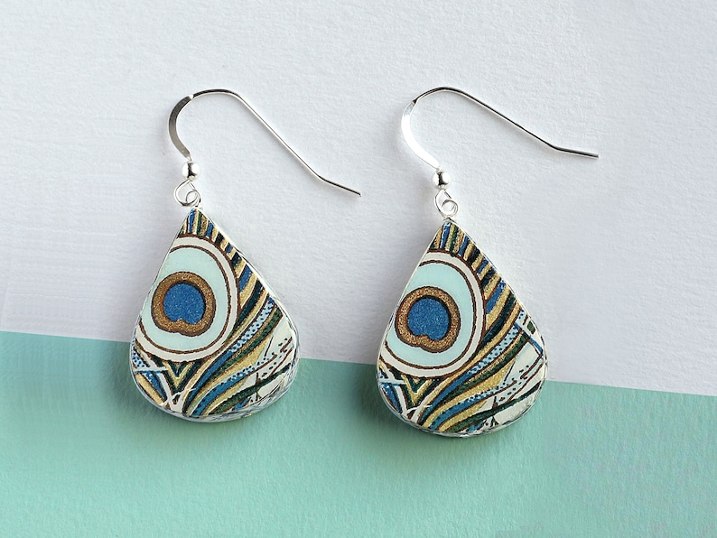 May include: A pair of silver teardrop earrings with a blue, green, and gold peacock feather pattern.