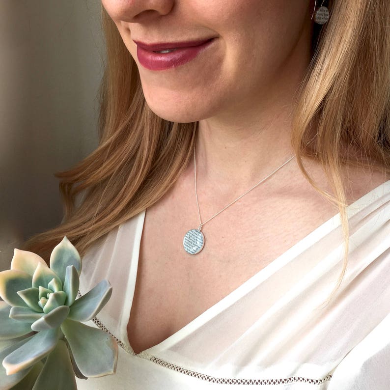 May include: A silver necklace with a round pendant featuring a textured design. The pendant is hanging on a silver chain.