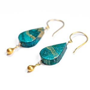 May include: Teal and gold teardrop shaped earrings with gold ball accents. The earrings are made of paper and have a unique, textured finish.