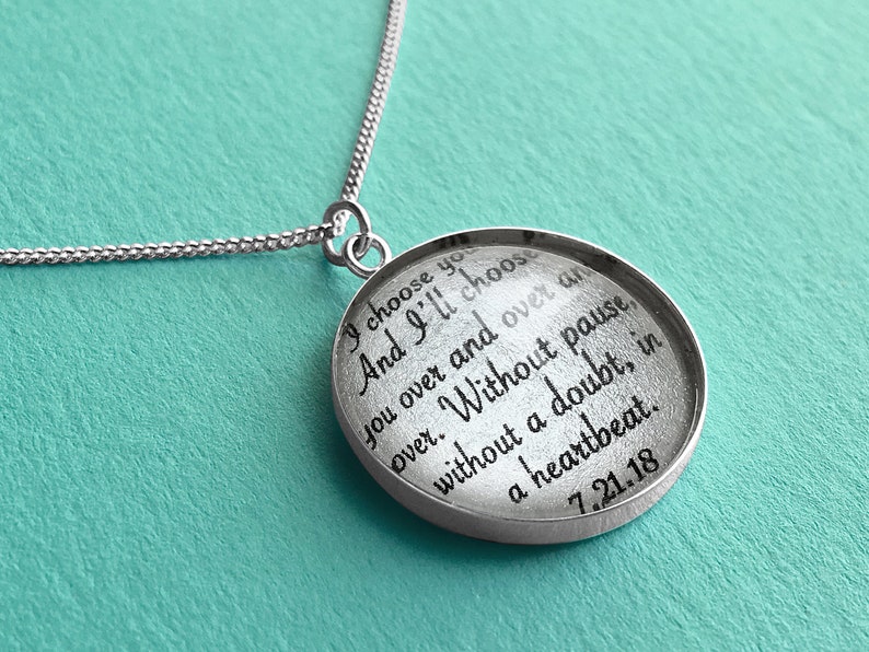 May include: A silver necklace with a round pendant that says "I choose you and I'll choose you over and over and over. Without pause without a doubt, in a heartbeat. 7.21.18"