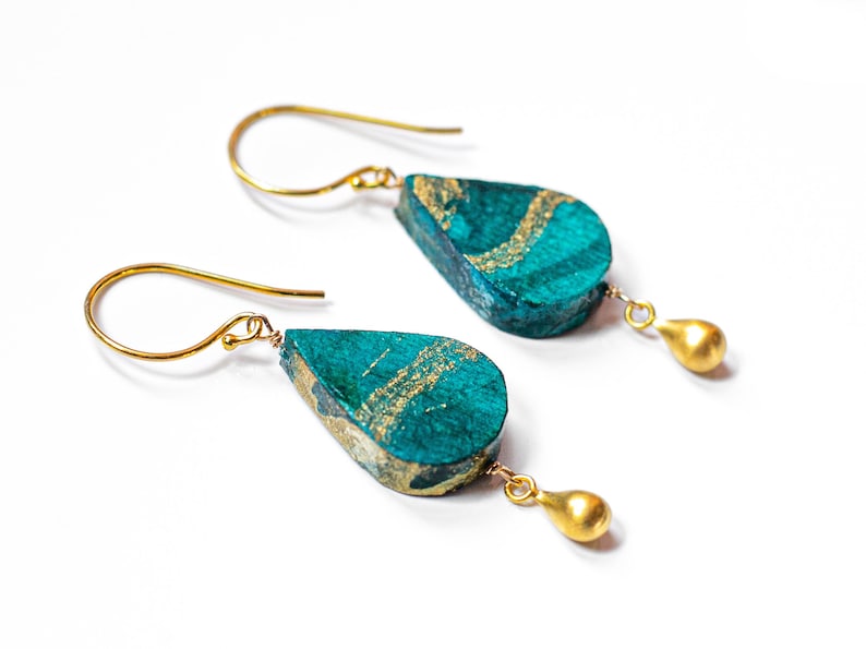 May include: Teal and gold teardrop shaped earrings with gold hooks. The earrings have a textured surface and a gold accent.