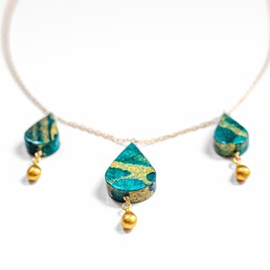 May include: A gold chain necklace with three teardrop-shaped pendants. The pendants are made of a green and gold material with a marbled pattern. Each pendant is accented with a small gold bead.