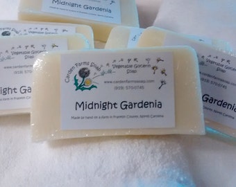 Può includere: Quattro saponette bianche con un'etichetta che recita "Garden Farms Soap - Vegetable Glycerin Soap" e "Midnight Gardenia" con un'immagine di dente di leone. Il sapone è fatto a mano in una fattoria a Pigeon Forge, Tennessee.