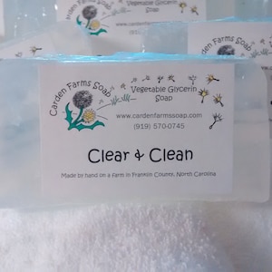 May include: A bar of clear, handmade soap with a white label that reads "Garden Farms Soap" with a dandelion graphic and the text "Vegetable Glycerin Soap" and "Clear & Clean". The label also includes the website address "www.gardenfarmssoap.com" and the phone number "(919) 570-0745". The soap is made by hand on a farm in Franklin County, North Carolina.