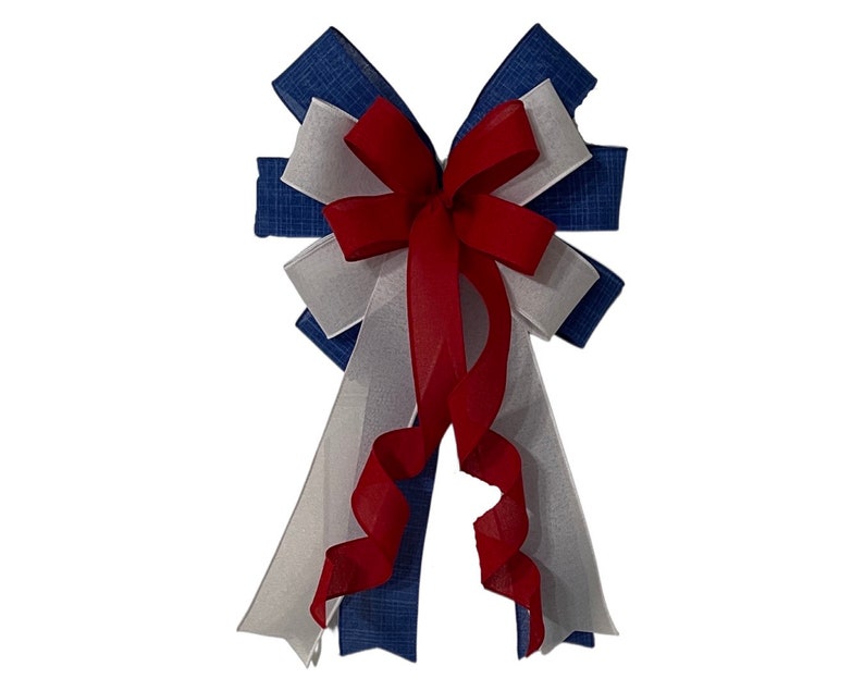 May include: A decorative bow featuring a patriotic color scheme. The bow is composed of blue, white, and red ribbons. The bow's design includes a central red bow and cascading ribbons in the same colors. Perfect for festive decorations.