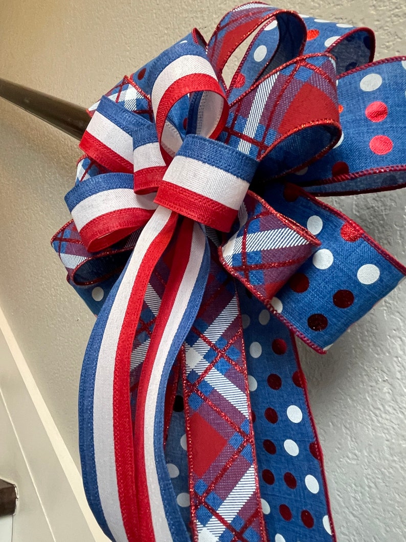 Puede incluir: Un lazo decorativo con colores patri&oacute;ticos. El lazo tiene cintas azules, blancas y rojas con lunares, rayas y patrones de cuadros. El lazo probablemente se utiliza para decoraci&oacute;n, posiblemente para una festividad o evento especial.