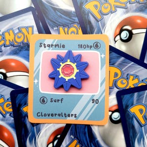 May include: A Starmie Pokémon card with a blue and red star-shaped design, 180 HP, and the text "Surf 90". The card is surrounded by other Pokémon cards.