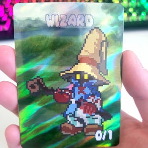 May include: A holographic trading card featuring a pixelated wizard character. The card has the word "WIZARD" in pixelated text at the top. The wizard is wearing a brown hat and blue robes. The card is marked "0/1" at the bottom.