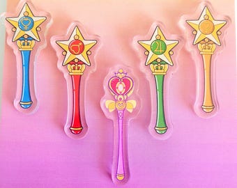 May include: Five colorful star-shaped wands with different symbols on the top. The wands are made of clear acrylic and have a pink, blue, red, green, and gold color scheme.