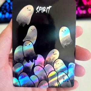 May include: A black card with the word "SPIRIT" in white script. The card features a holographic design of several cartoon ghosts with smiling faces. The ghosts are in shades of white, grey, and iridescent colours. The bottom right corner has the number "2/2".