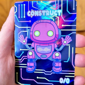 May include: A holographic card featuring a pink robot with the word "CONSTRUCT" in white. The robot has large yellow eyes, headphones, and a sound wave graphic on its chest. The card has a blue circuit board design and the numbers "0/0".