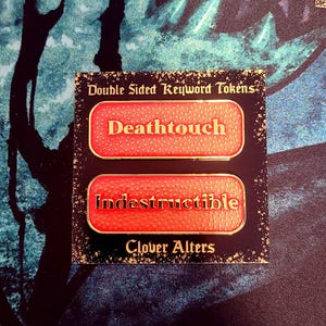 May include: Double-sided keyword tokens with the words "Deathtouch" and "Indestructible" in red lettering. The tokens have a gold border and are on a black background. The text "Clover Alters" is also visible.