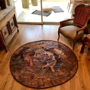 Könnte beinhalten: Ein runder, brauner Teppich aus Lederresten. Der Teppich hat ein kreisförmiges Muster aus verschiedenen Brauntönen von Lederstücken. Der Teppich liegt auf einem Holzboden in einem Raum mit Möbeln.