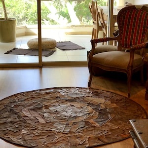 Könnte beinhalten: Ein runder, brauner Teppich aus Lederresten. Der Teppich hat ein kreisförmiges Muster und liegt auf einem Holzboden. Im Hintergrund steht ein Stuhl mit einem gestreiften Stoffbezug.