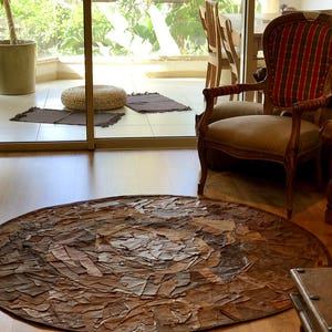 Könnte beinhalten: Ein runder, brauner Teppich aus Lederresten. Der Teppich hat ein kreisförmiges Muster und liegt auf einem Holzboden.