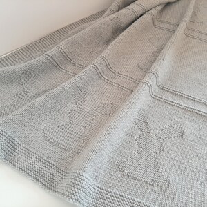 Könnte beinhalten: Eine graue gestrickte Babydecke mit einem strukturierten Muster. Die Decke ist gefaltet und hat ein weiches, gemütliches Aussehen.
