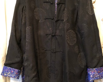 May include: Black silk jacket with a mandarin collar and frog closures. The jacket is decorated with a repeating pattern of black circles with intricate designs. The lining is a vibrant blue and gold floral pattern.