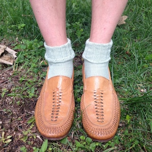 May include: A pair of brown leather loafers with woven detailing. The loafers are worn with light green socks.