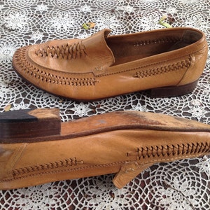 May include: A pair of tan leather loafers with a braided design on the toe and a brown leather sole.