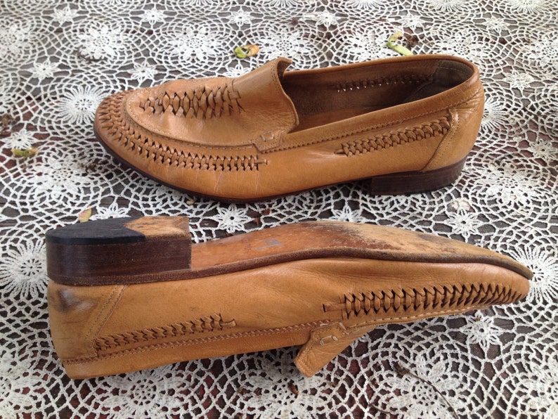 May include: A pair of tan leather loafers with a braided design on the toe and a brown leather sole.