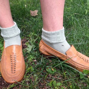 May include: A pair of brown leather loafers with a woven design. The loafers are worn with light green socks.