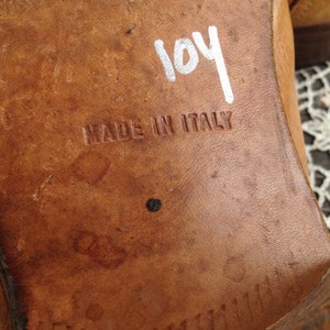 May include: Close-up of the bottom of a brown leather shoe with the text "MADE IN ITALY" and the number "104" written in white marker.