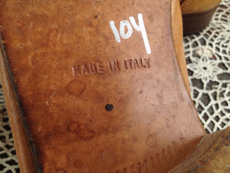 May include: Close-up of the bottom of a brown leather shoe with the text "MADE IN ITALY" and the number "104" written in white marker.