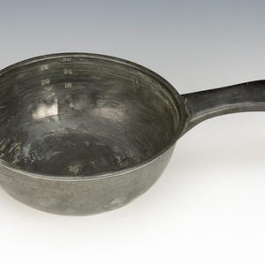 May include: A dark gray metal measuring cup with a handle. The interior has measurement markings for 8, 16, 20, 24, and 32. The handle is attached to the side of the cup.