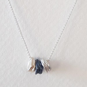 Puede incluir: Un collar de cadena de plata con un colgante hecho de anillos apilados de plata, oro y negro.