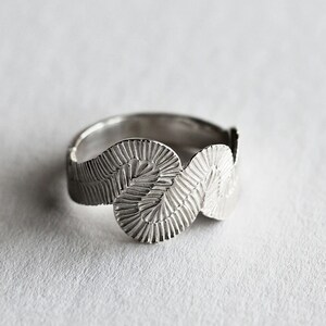 Peut inclure: Une bague en argent avec un design ondulé texturé. La bague est composée de trois formes arrondies reliées.