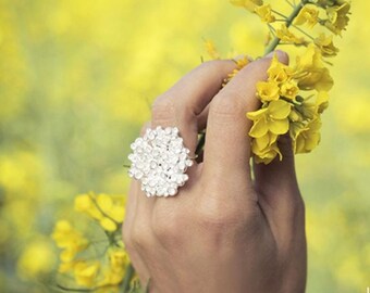 May include: A hand wearing a silver ring with a cluster of small white stones, smelling a bouquet of yellow flowers. The flowers are in focus, while the hand and background are blurred. The text "maa bijoux" and "ecu.an1301" are visible in the bottom right corner of the image.