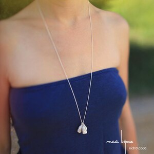 May include: A silver necklace with a pendant featuring three small, textured, silver teardrop shapes. The necklace is worn by a person with a blue strapless top.