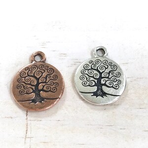 Puede incluir: Dos abalorios plateados con un dise&ntilde;o de &aacute;rbol de la vida. Un abalorio es de color cobre y el otro es plateado.