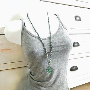 May include: A 6mm knotted mala necklace featuring small, mottled blue-green beads and a translucent, teardrop-shaped pendant with an embossed figure. The text 'Example of 6mm knotted Mala' is visible at the top of the image.