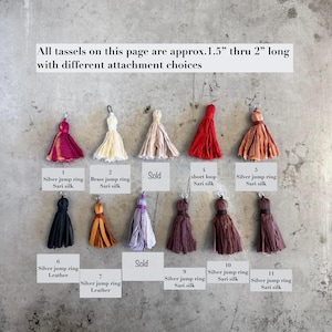 Op de afbeelding: Een collectie van elf kwastjes in diverse kleuren, waaronder magenta, wit, beige, rood, oranje, zwart en bruin. Elk kwastje is gelabeld met een nummer en type bevestiging, zoals een zilveren ringetje, messing ringetje of een lusje.