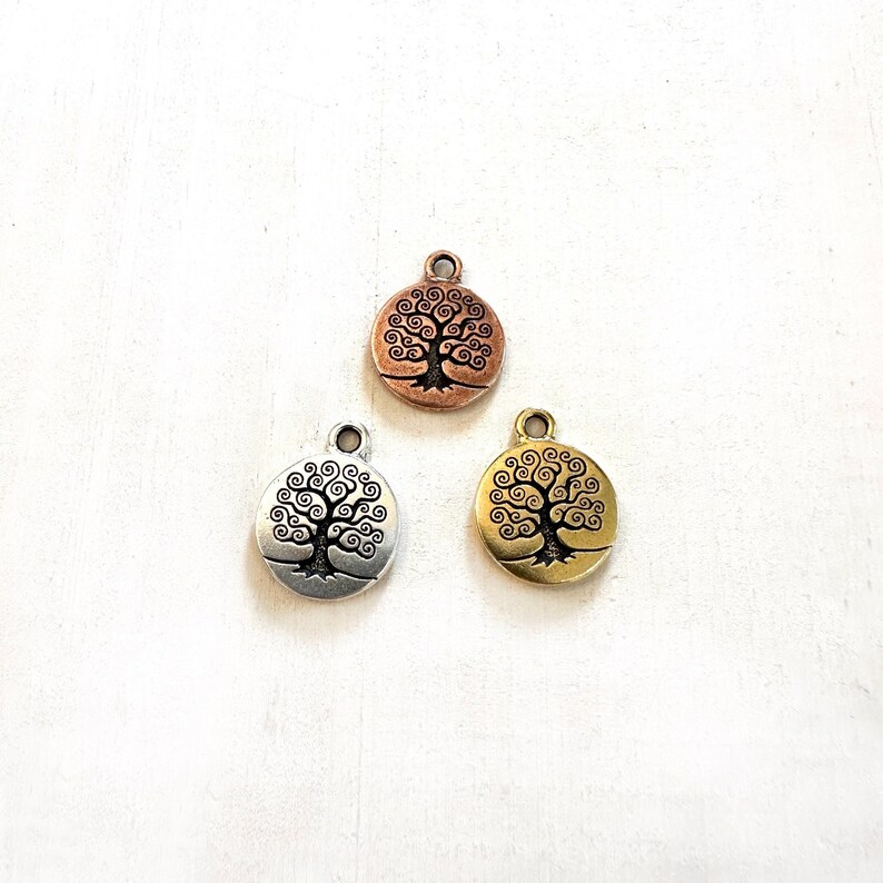 Puede incluir: Tres abalorios de metal con forma de &aacute;rbol de la vida. Los abalorios son de plata, oro y cobre.